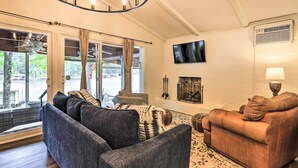 A living room with a grey sofa, a brown sofa, a chandelier, a fireplace, and a large window with curtains. - Eatonton Getaway on Lake Sinclair w/ Dock! (Eatonton)
