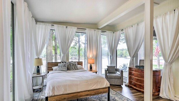 A bedroom with a bed, bedside tables, a chair, a dresser, and large windows with curtains. - Eatonton Getaway on Lake Sinclair w/ Dock! (Eatonton)