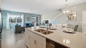 A modern kitchen with a central island, double sinks, and a dining area with a chandelier. - Champions Gate by CozyKey (Davenport)