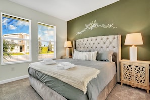 A bedroom with a large bed, two bedside lamps, a decorative wall piece, and a view through the window. - Champions Gate by CozyKey (Davenport)