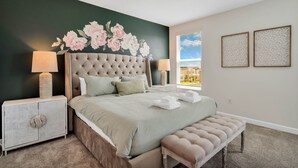 A bedroom with a tufted headboard, a large bed with a green bedspread, two bedside lamps, a nightstand, a bench, and a window with blinds. - Champions Gate by CozyKey (Davenport)