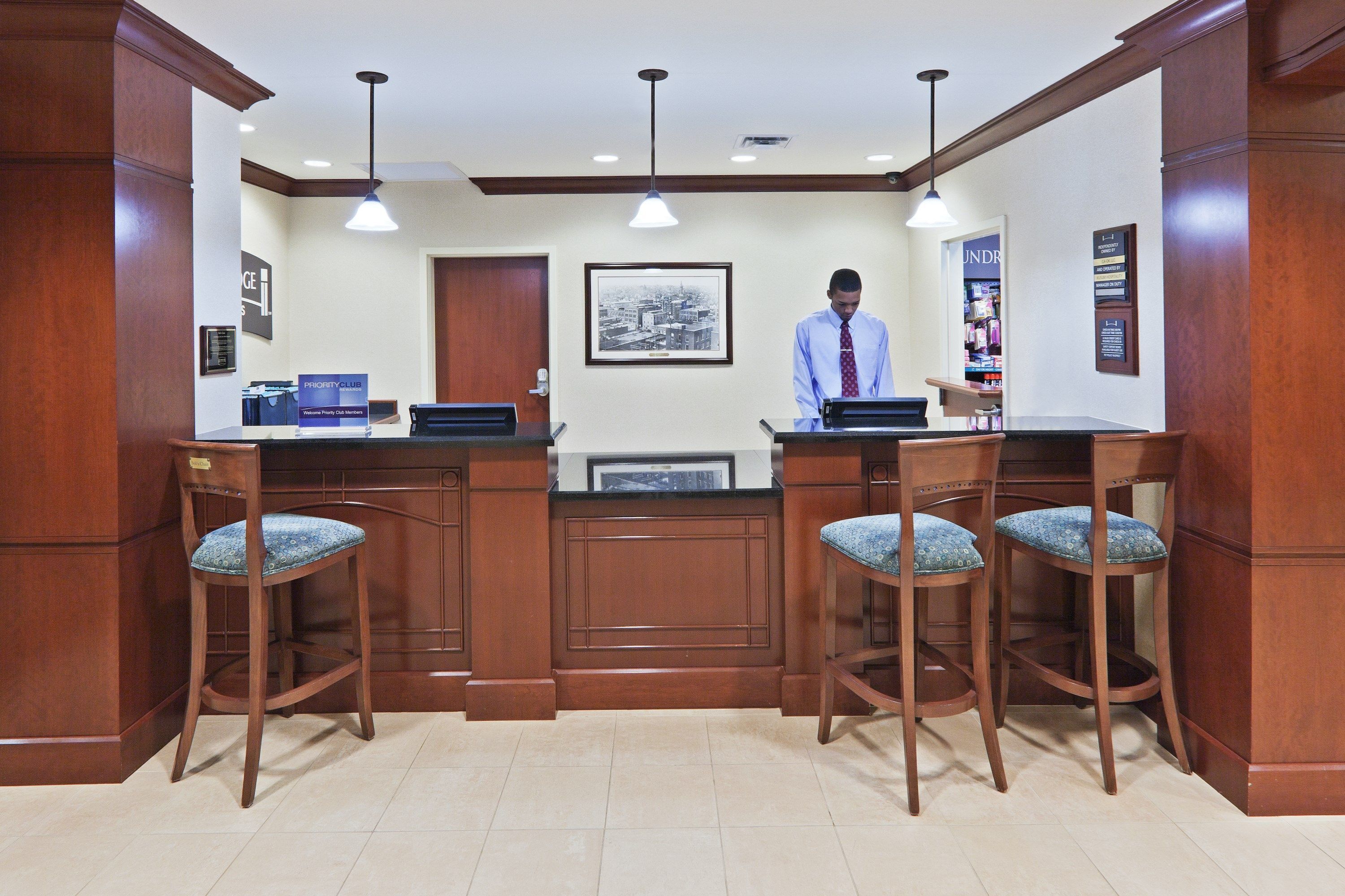 A reception area with wooden furniture, a framed cityscape, and a man at the counter.