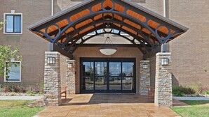 A building entrance with a covered porch, stone pillars, and a large glass door. - 1 Bedroom | Free Breakfast, Pool Access (Oklahoma City)