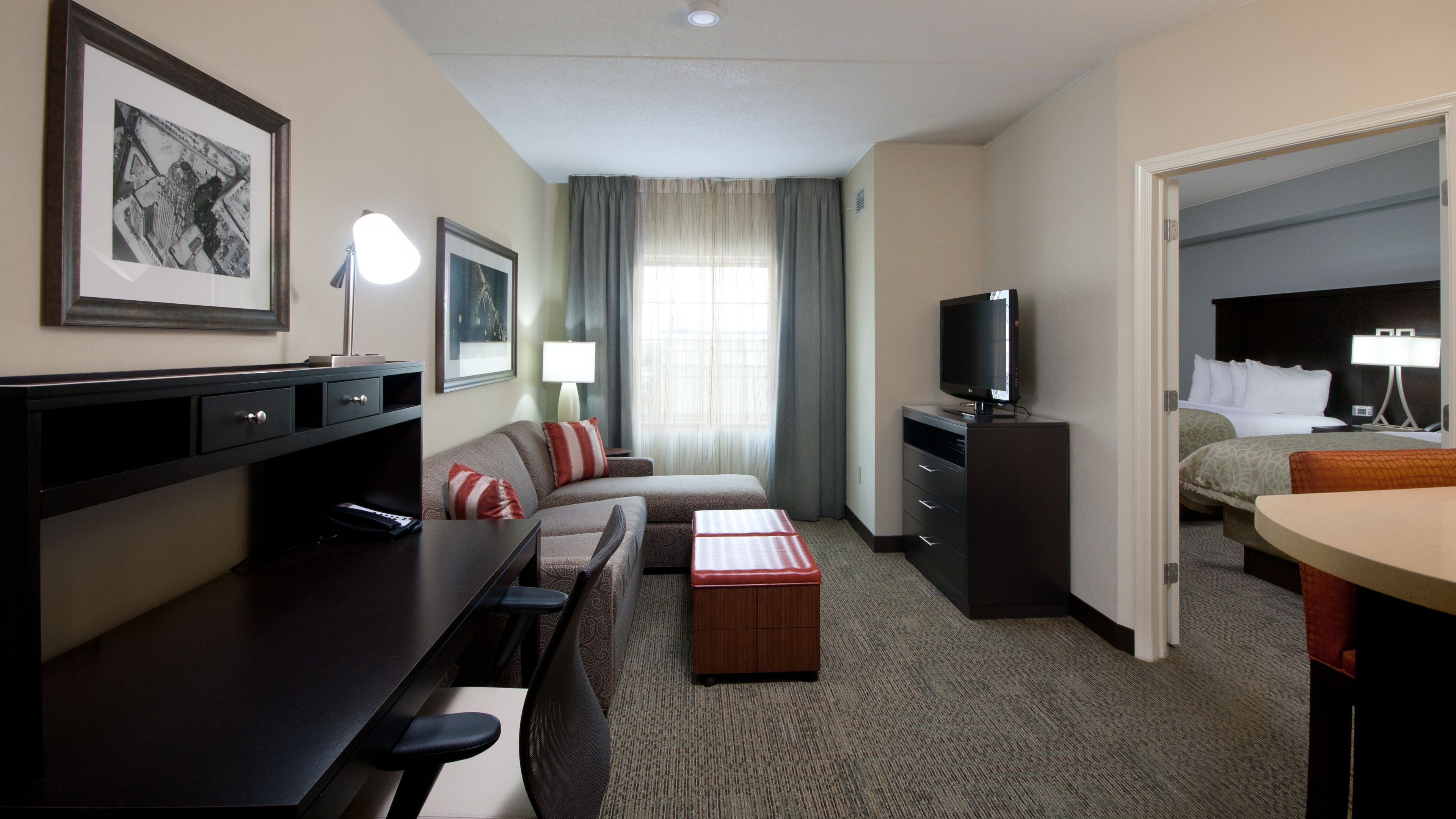 A hotel room with a bed, a desk with a computer, a TV, a sofa, and a small table.
