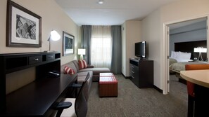 A hotel room with a bed, a desk with a computer, a TV, a sofa, and a small table.