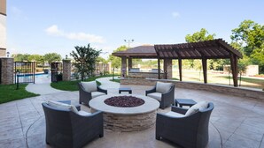 Un espace extérieur aménagé en terrasse, avec un foyer circulaire entouré de meubles en osier.