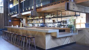 Un bar con mostrador de madera, taburetes y una variedad de botellas y vasos.