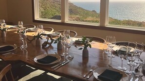 A dining table set for six with a view of the ocean through large windows. - Timber Cove Resort (Jenner)
