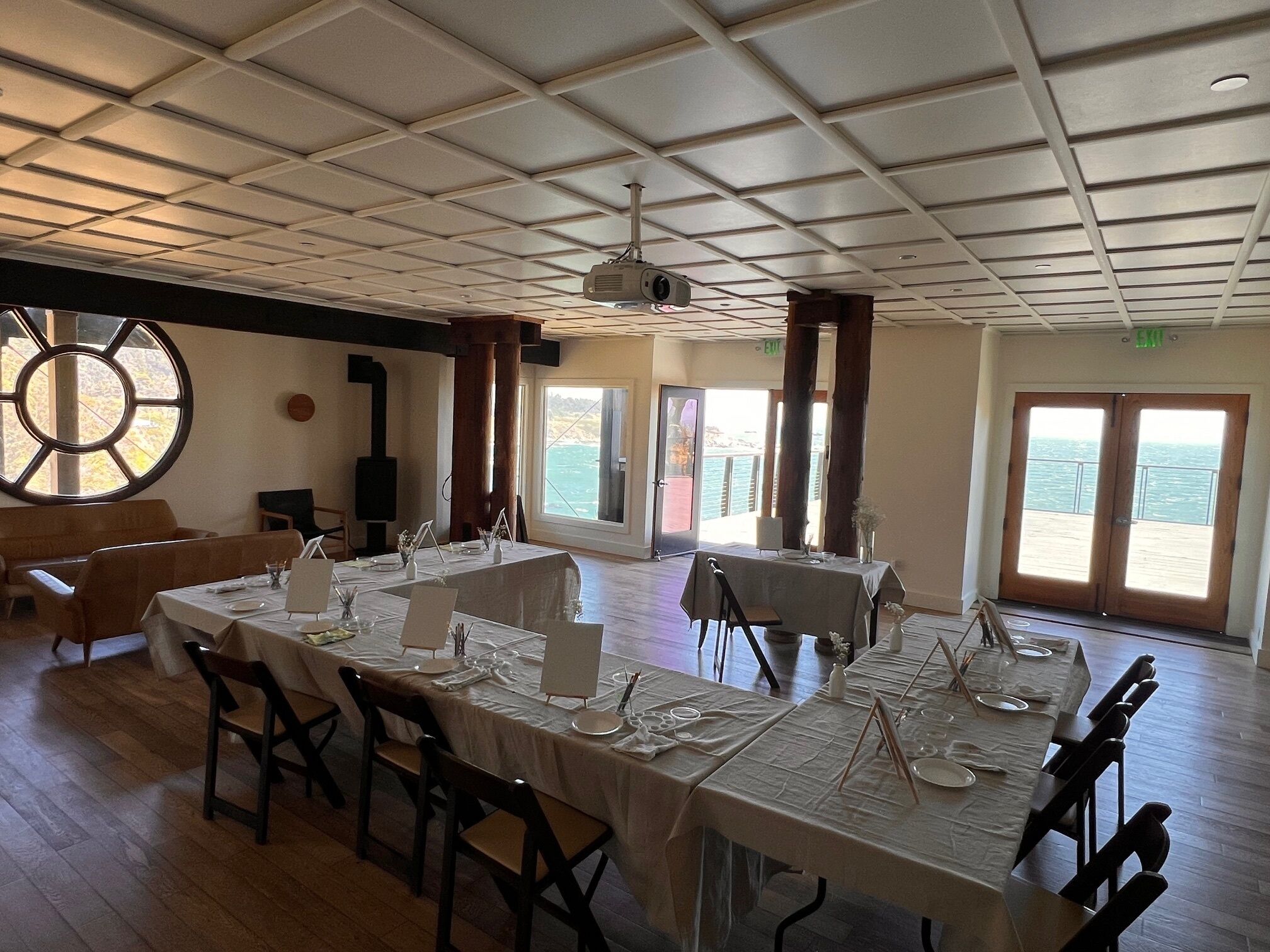 Un espace repas avec des tables dressées pour le repas, de grandes fenêtres et une vue sur la mer.