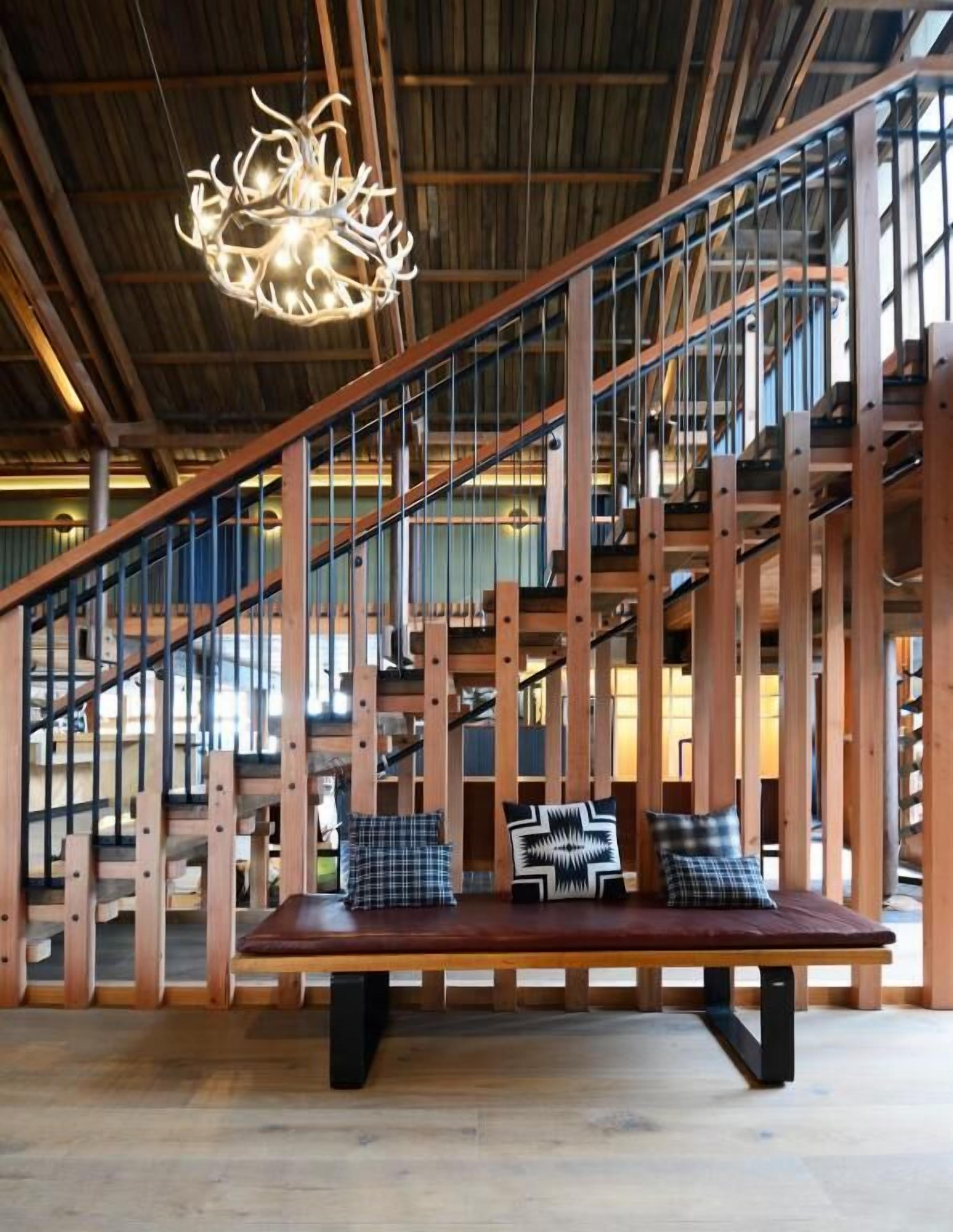 Un interior amplio con una escalera de madera, un banco con almohadones y una lámpara original.