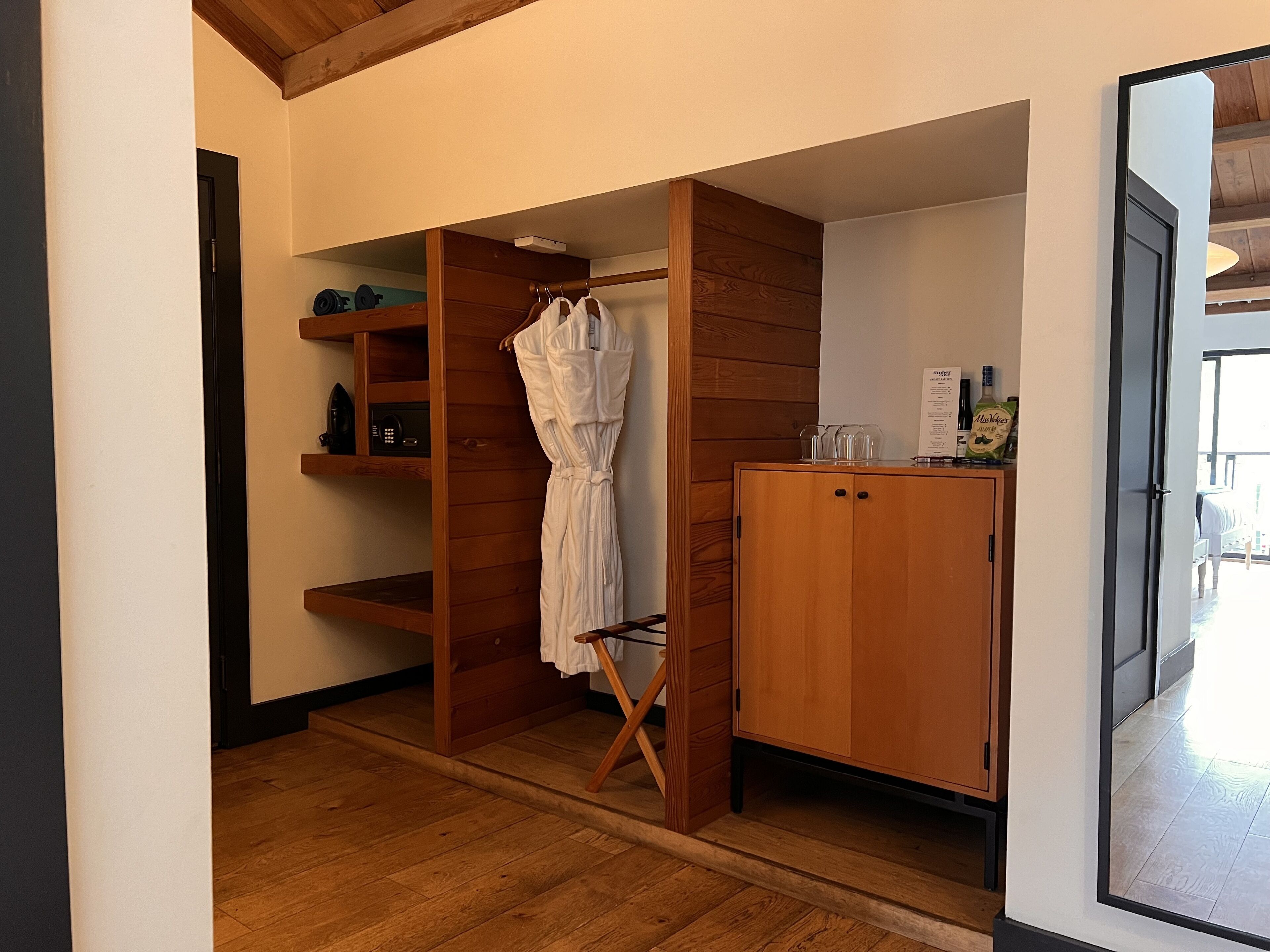 Ein kleines Zimmer mit einem Holzschrank, einer kleinen Ablagefläche mit Gegenständen und einem weißen Bademantel an einem Gestell.