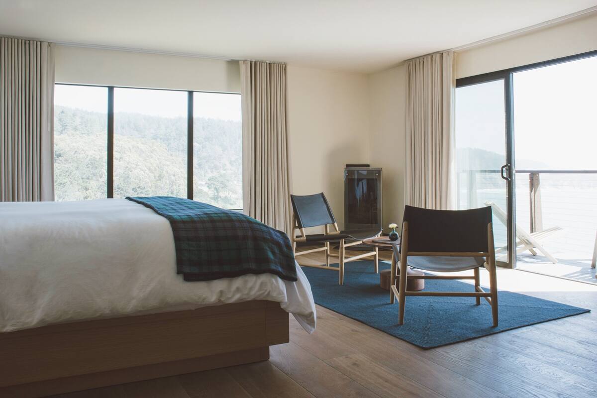 Quarto de hotel com cama grande, uma cadeira, televisão e varanda com vista para as montanhas.