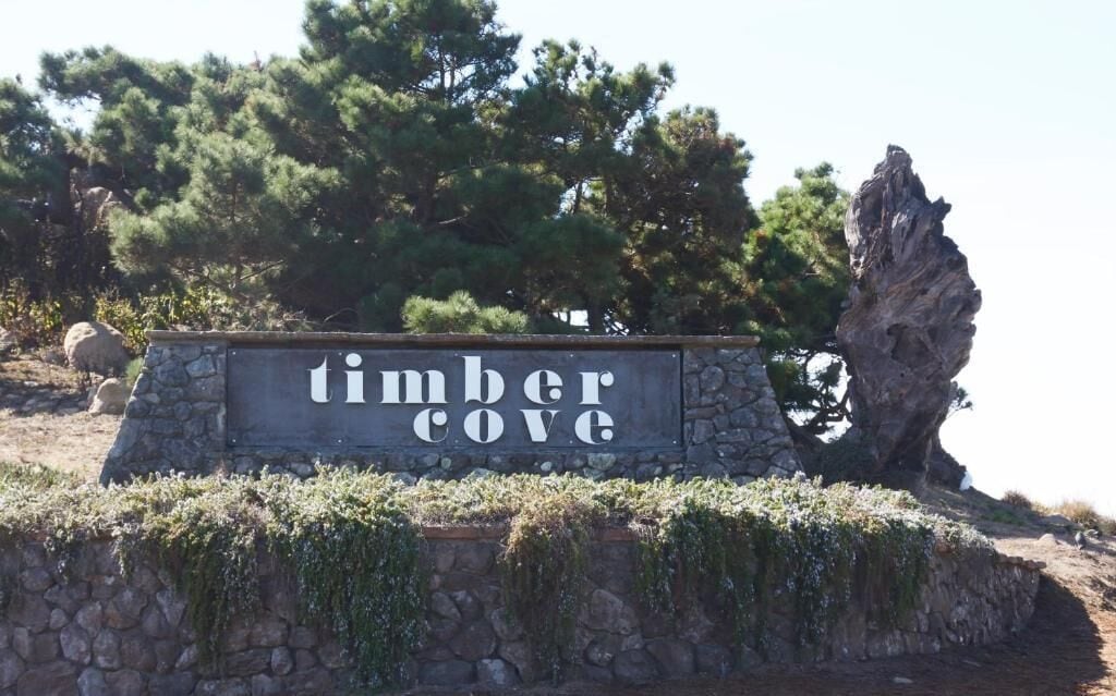 A stone sign with the text "timber cove" surrounded by natural scenery.