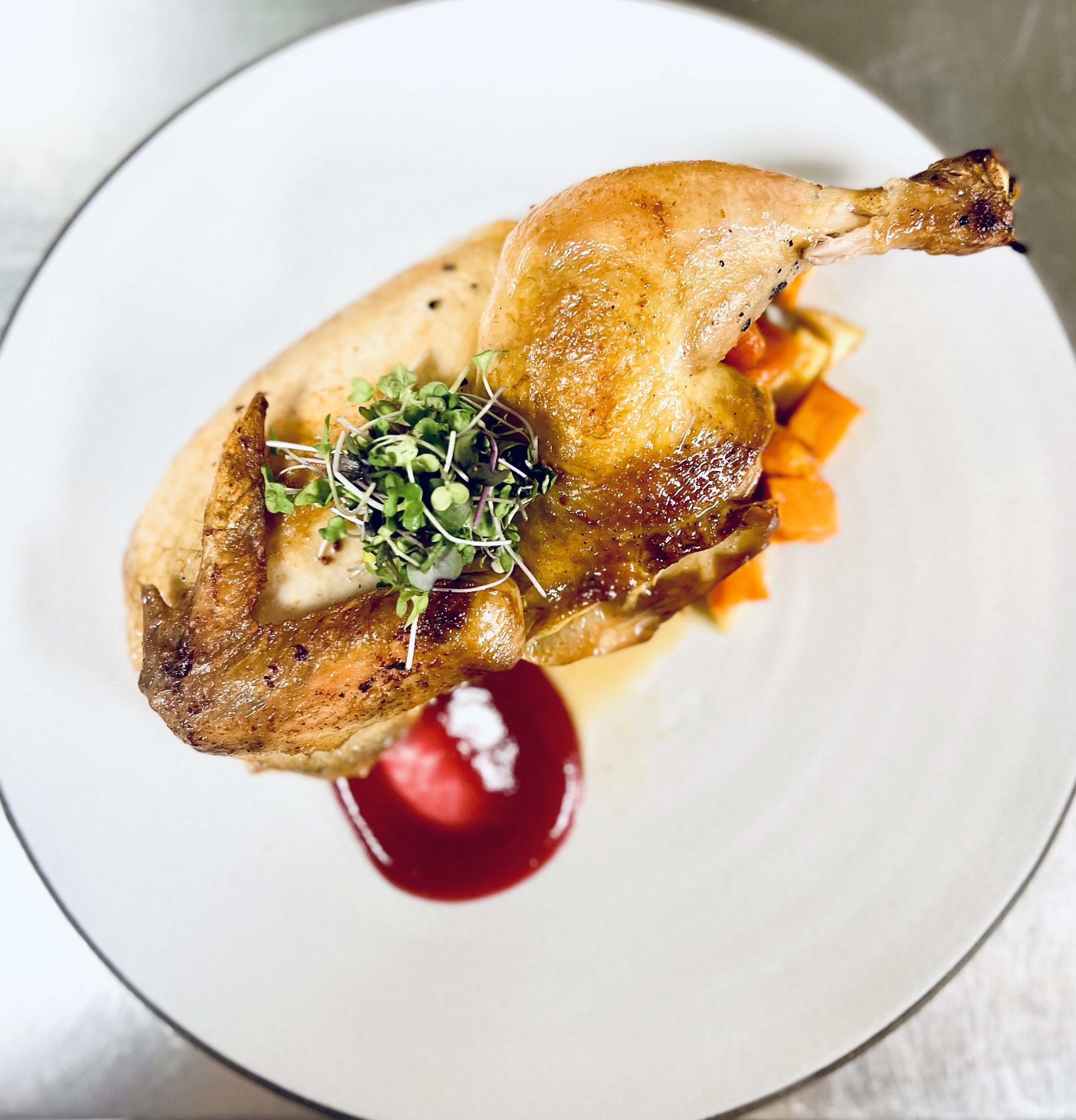 A roasted chicken with sprouts and a sauce on a plate.