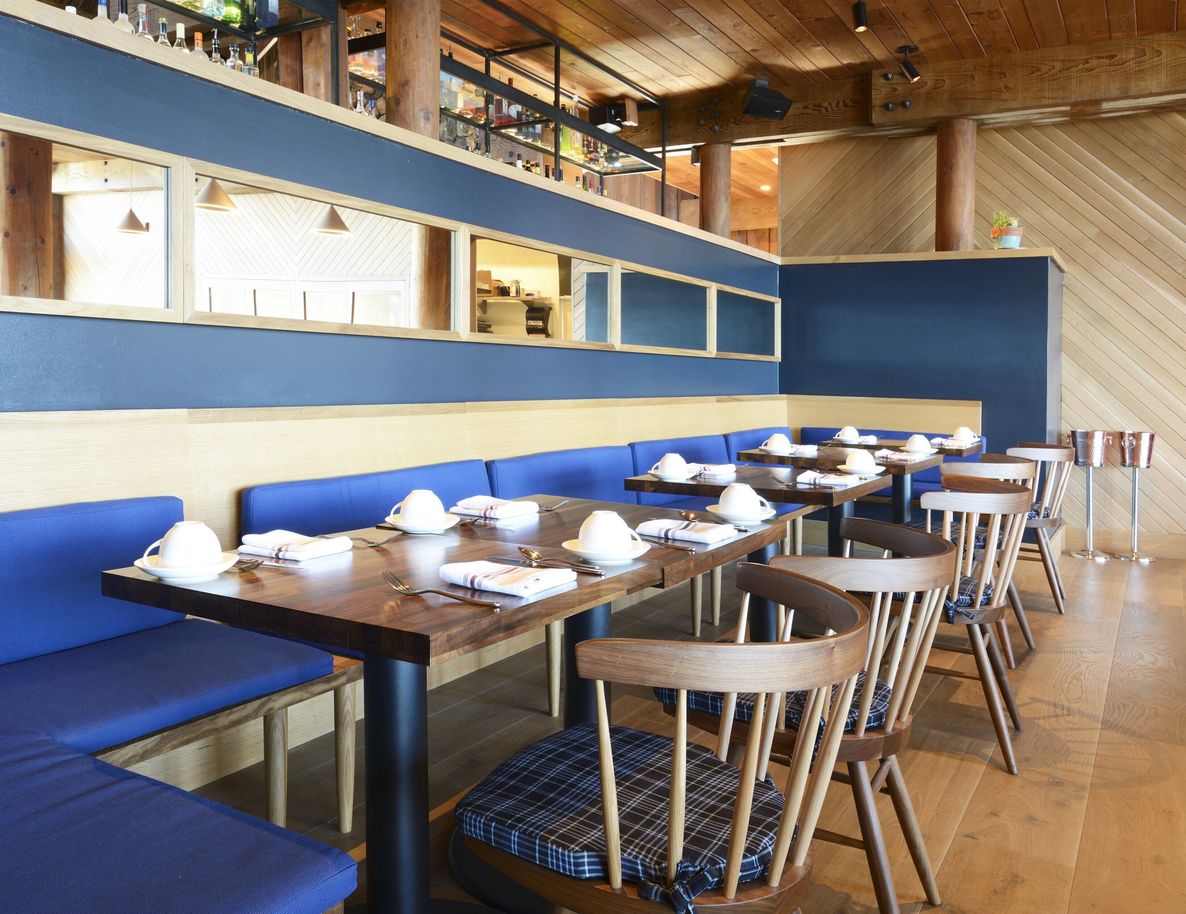 A restaurant with wooden tables, blue cushioned booths, and a high ceiling with exposed beams.