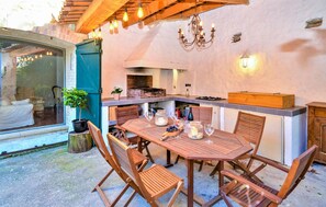 An outdoor dining area with a wooden table and chairs, a built-in grill, and a view through a glass door. - Stunning home in Mornas (Mornas)
