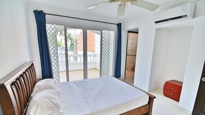 Quarto com cama, cómoda vermelha, ventoinha no teto e vista para a varanda.