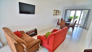 Uma sala de estar com um sofá marrom, um sofá vermelho e uma TV fixada na parede.