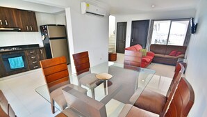 Uma sala de estar moderna com uma mesa de jantar de vidro, cadeiras de couro marrom, um sofá vermelho e uma área de cozinha com armários de madeira escura e uma geladeira de aço inoxidável.