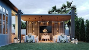An outdoor dining area with multiple tables, overhead lighting, and a backdrop of vertical wooden slats.