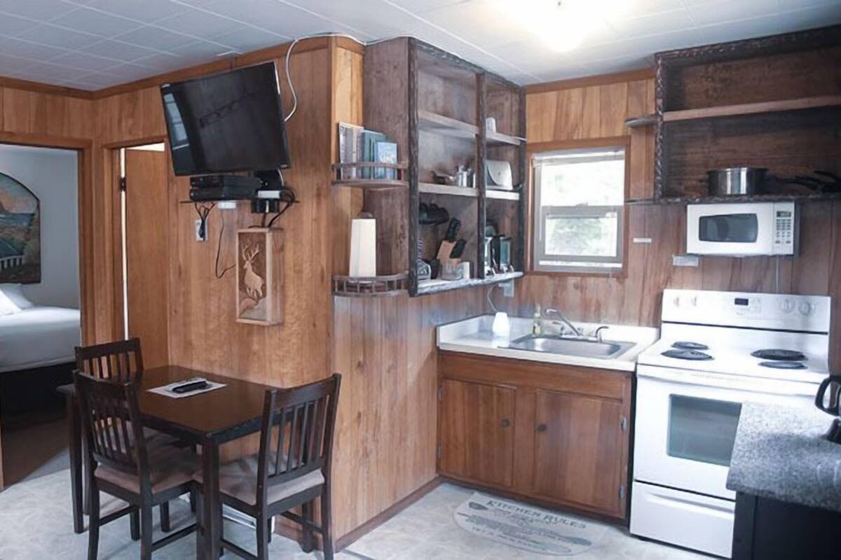 A compact kitchen with wooden cabinets, a microwave, a stove, and a dining area with a table and chairs.