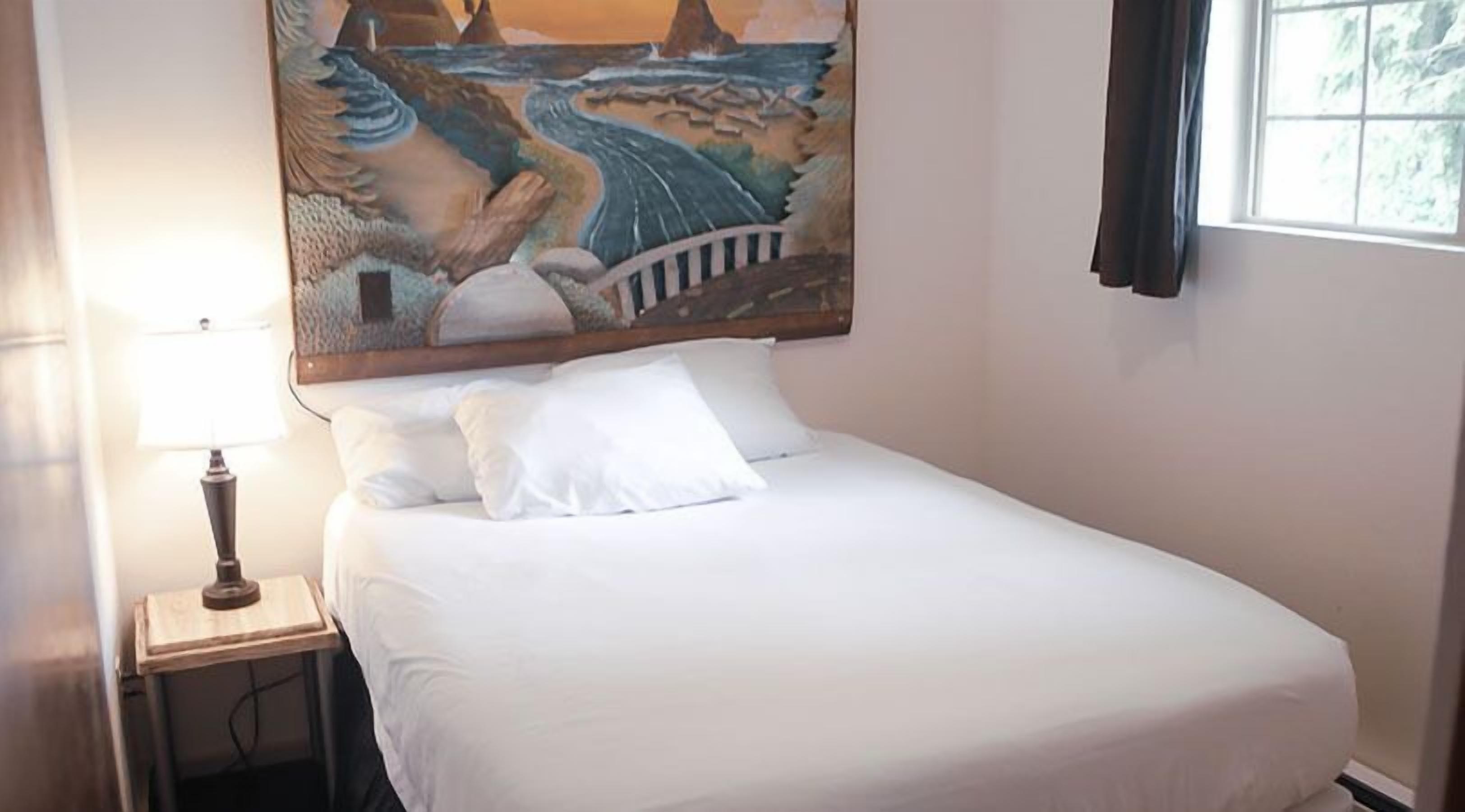 A neatly made bed with white linens in a room with a large painting above it.