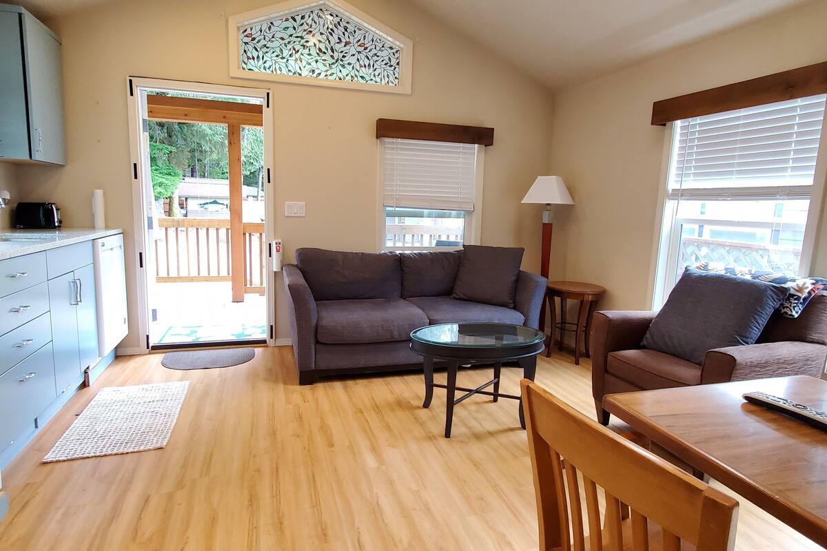 A compact living space with a kitchenette, a sofa, a dining table, and a window with blinds.