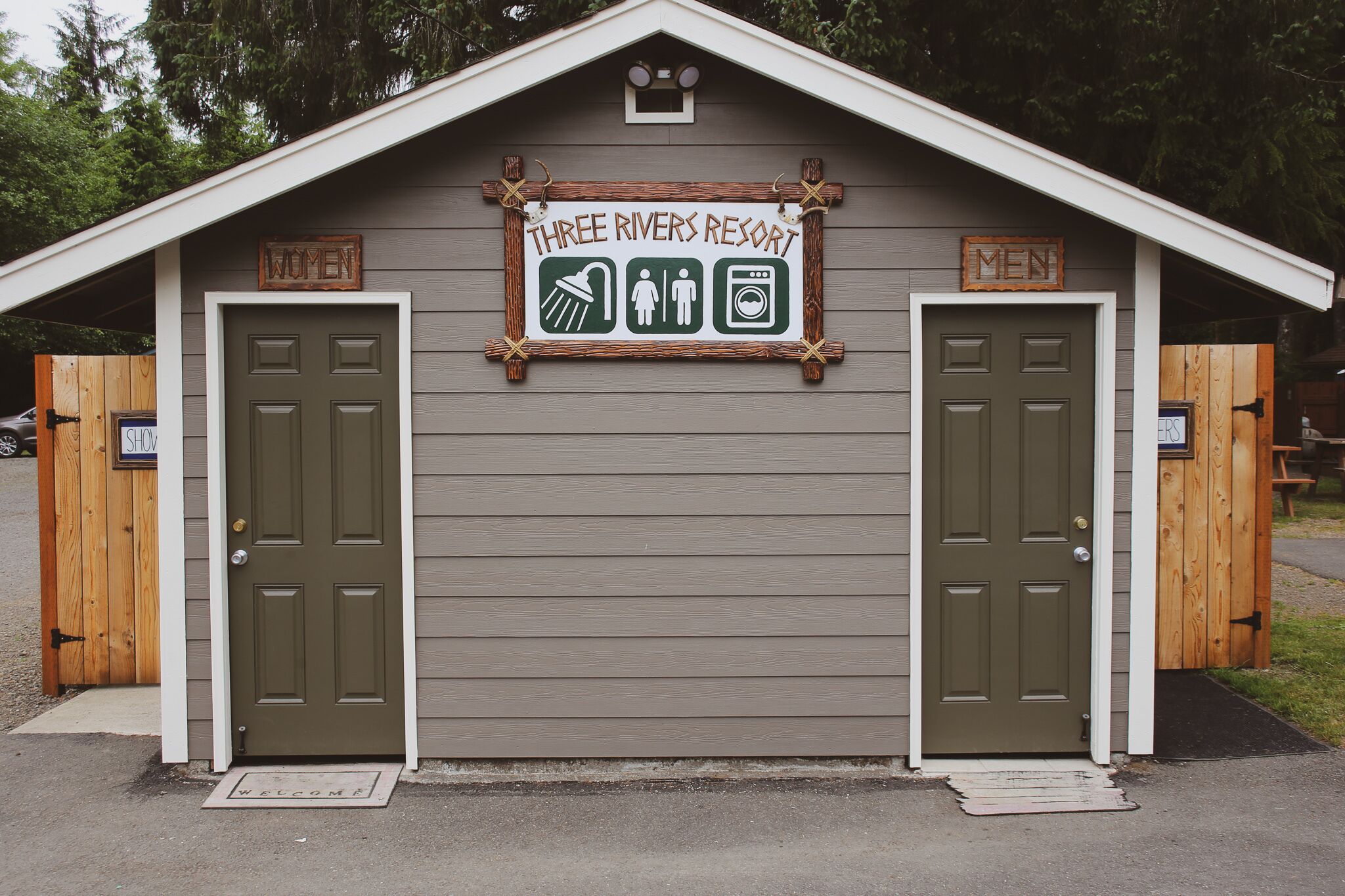 A small building with two doors labeled "WOMEN" and "MEN" and a sign above stating "Three Rivers Resort".