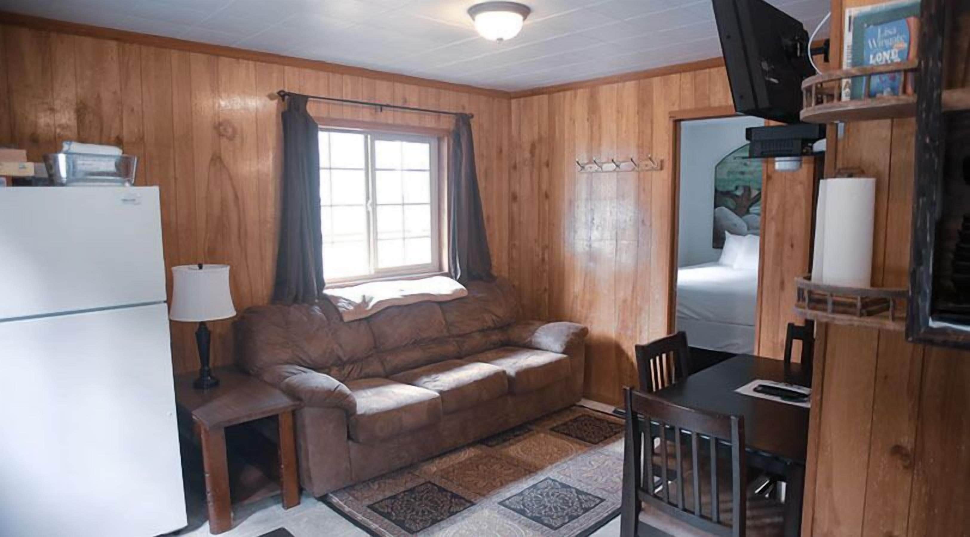 Una habitación compacta con interior de madera, un sofá, una mesita, un refrigerador y un televisor fijado a la pared.