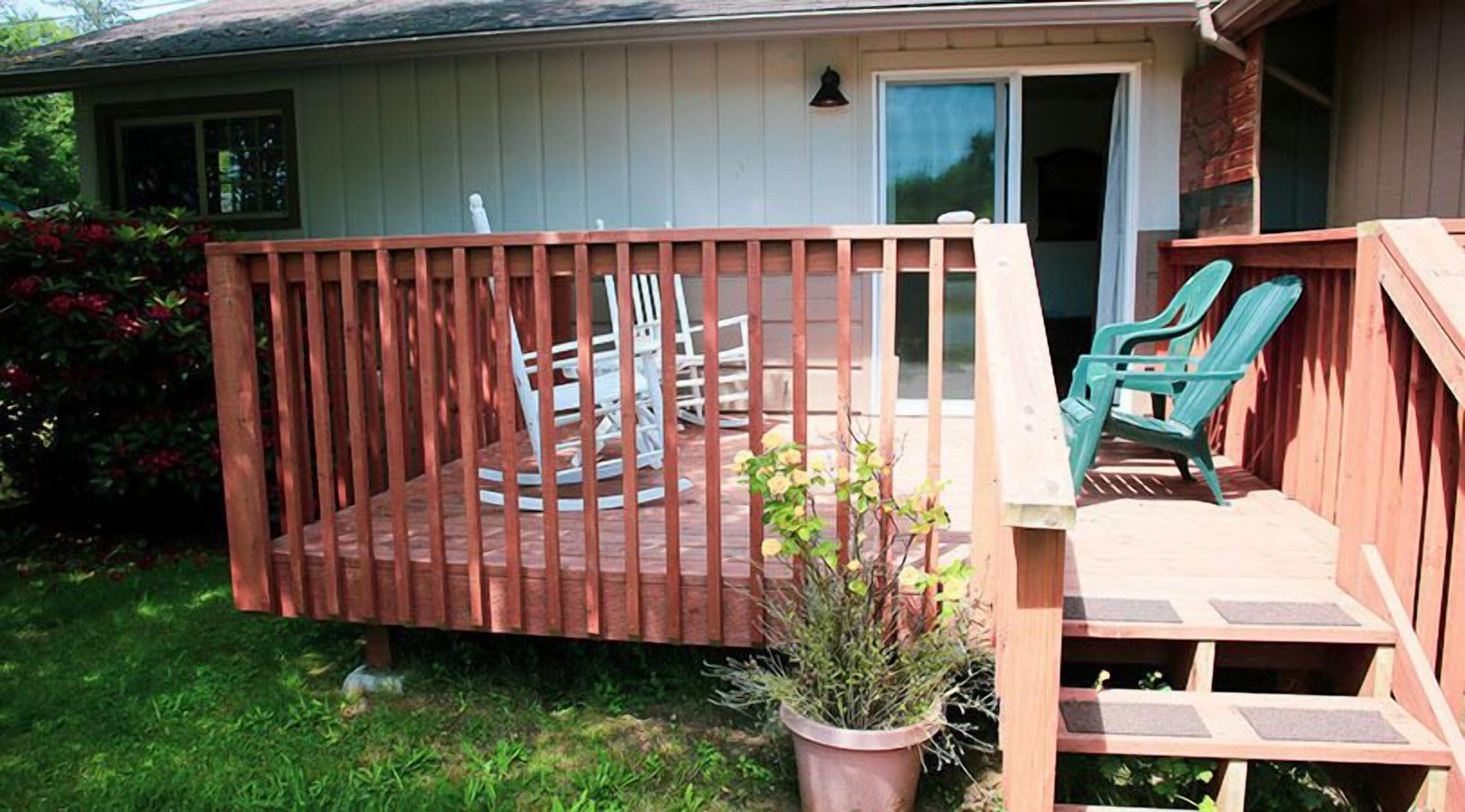 A wooden deck with a small table and chairs, a potted plant, and a sliding glass door leading to a covered area.