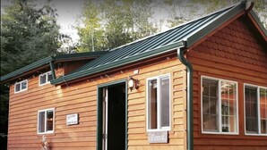 Une cabane en bois avec un toit vert, une pancarte indiquant « Forêt », et deux chaises à l’extérieur.