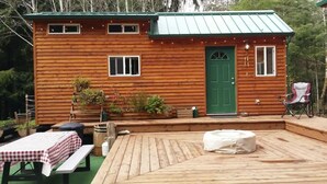 A wooden cabin with a green door, a deck, a table with a checkered tablecloth, and a chair. - 3 Rivers Resort and Guide Service (Forks)