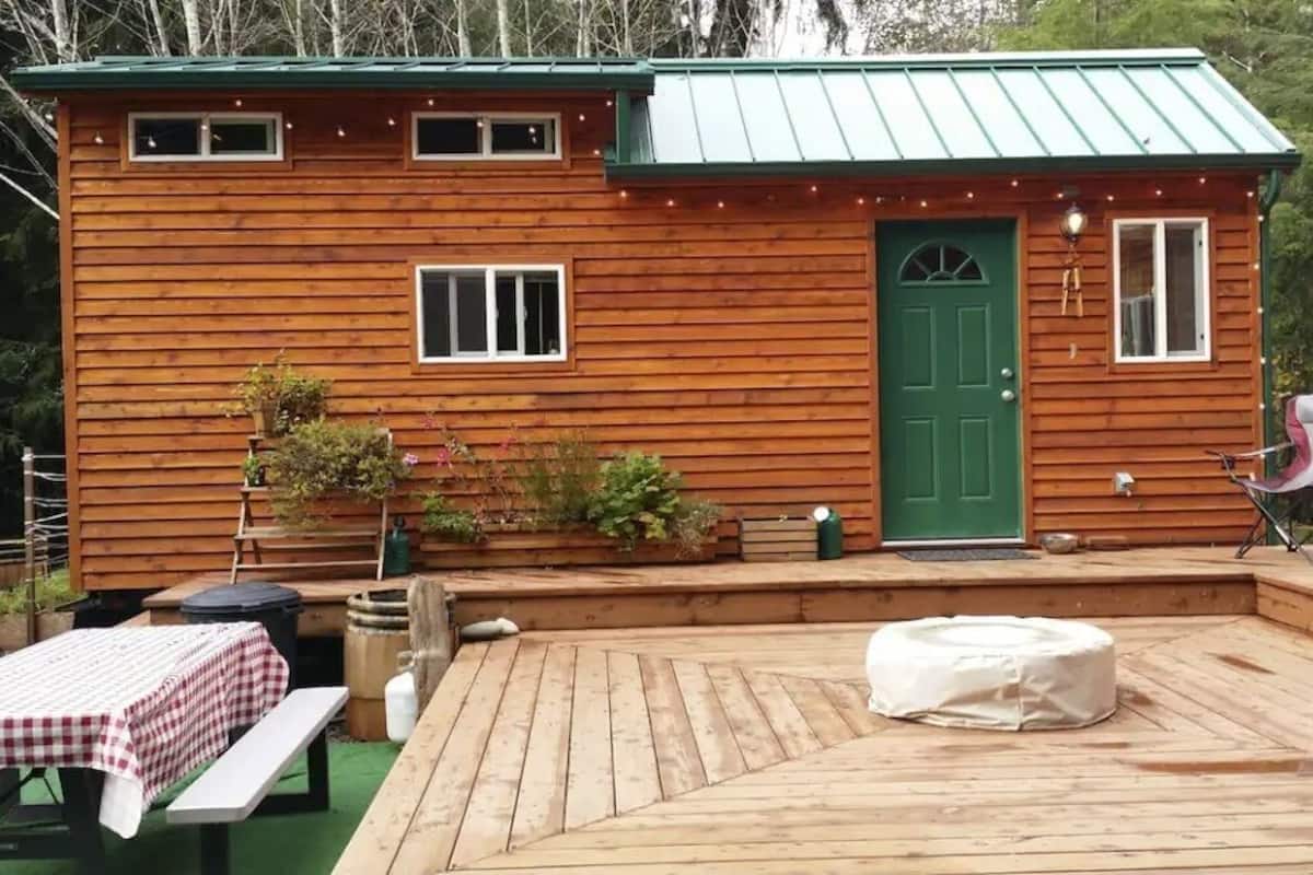A wooden cabin with a green door, a deck, a table with a checkered tablecloth, and a chair.