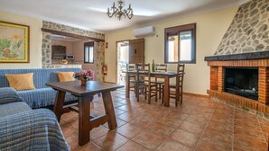 Un salon avec une cheminée en pierre, un coin repas avec une table et des chaises, et un canapé bleu agrémenté de coussins.