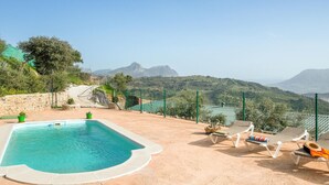 Une piscine avec vue sur les montagnes, entourée d’une clôture et de chaises longues.