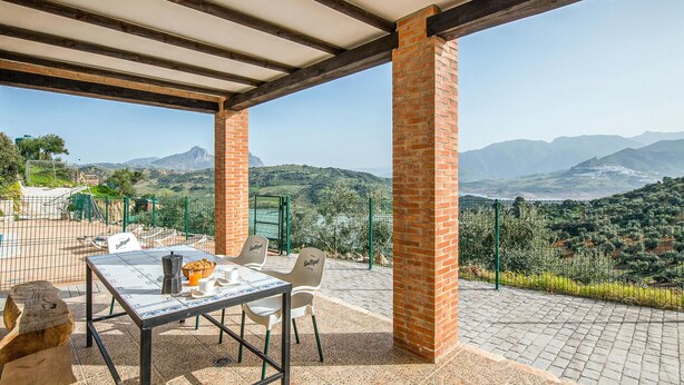 Un espace extérieur abrité, avec une table et des chaises, offrant une vue sur un paysage montagneux.