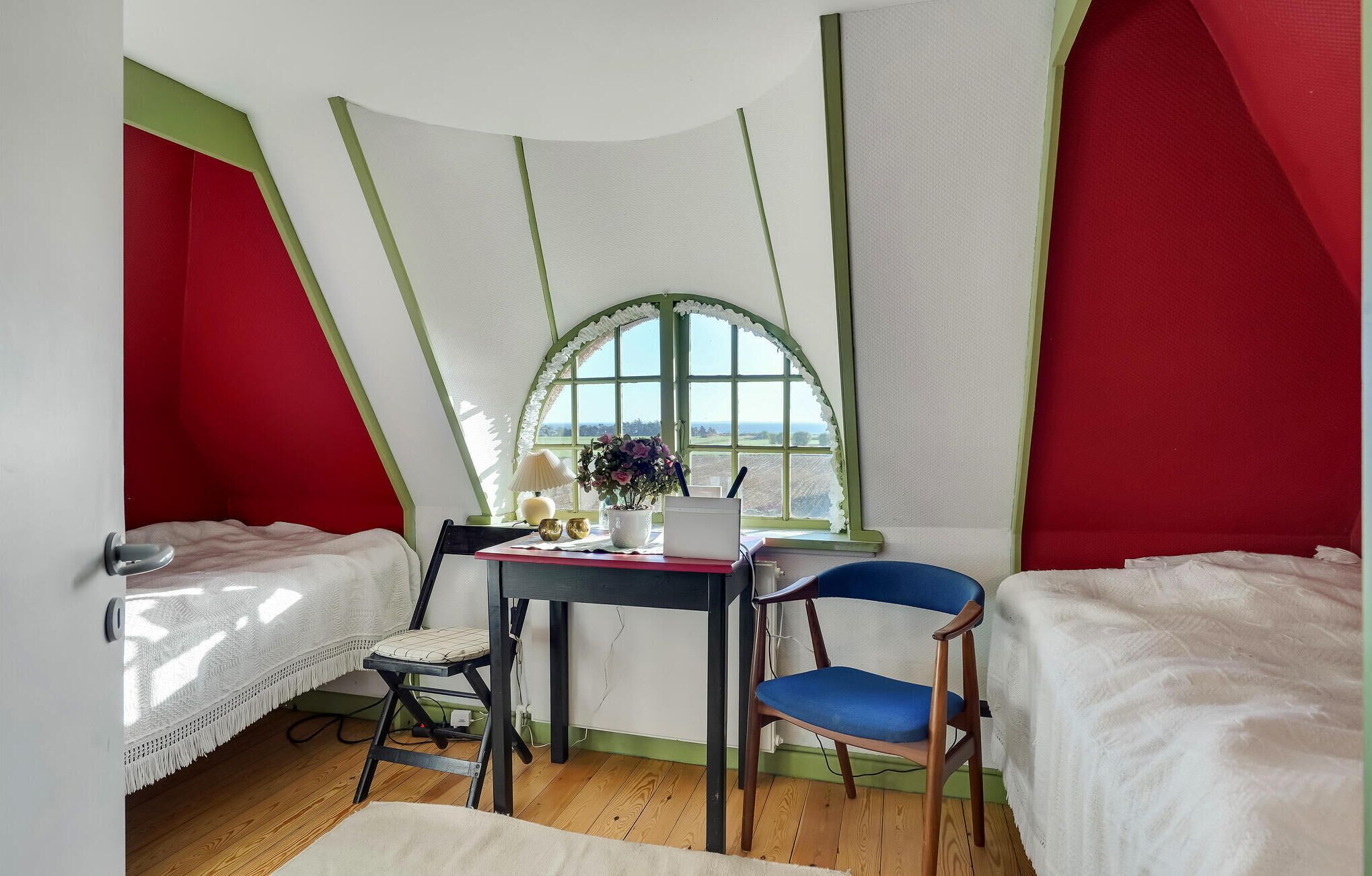 Ein gemütliches Zimmer mit Schreibtisch, zwei Stühlen, einem Fenster mit Aussicht und einem Bett.
