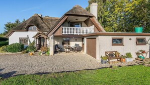 A two-story house with a thatched roof, a balcony, and a gravel driveway.