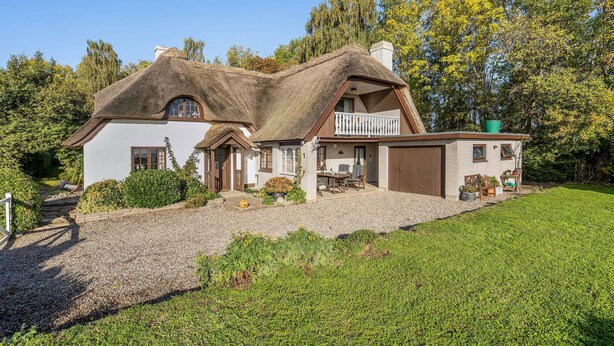 A house with a thatched roof, a wooden balcony, and a gravel driveway.