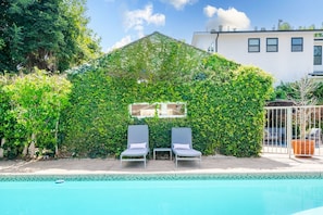 A pool area with two lounge chairs and a covered seating area with a view of the pool.