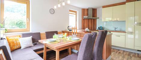 A modern kitchen with wooden cabinets, a dining area with a wooden table and chairs, and a view of the outdoors through a window.