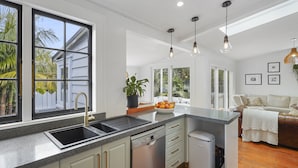 A modern kitchen with a built-in dishwasher, a sink, and a countertop. There is a dining area with a couch and a coffee table. - Tropical Paradise -Pool - Spa - Spacious (Auckland)