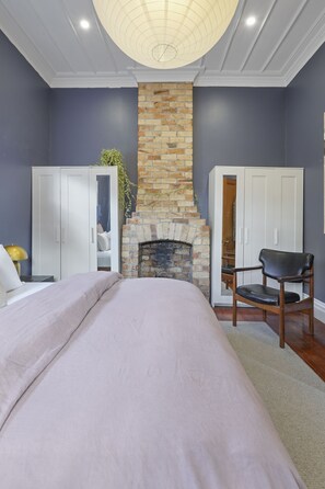 A bedroom with a bed, a stone fireplace, a wardrobe, and a chair. - Tropical Paradise -Pool - Spa - Spacious (Auckland)