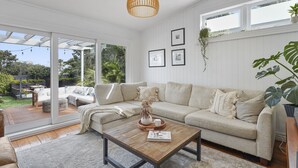 A modern living room with a sofa, coffee table, and hanging plants. - Tropical Paradise -Pool - Spa - Spacious (Auckland)