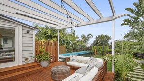 A wooden deck with outdoor furniture, a pool, and lush greenery. - Tropical Paradise -Pool - Spa - Spacious (Auckland)