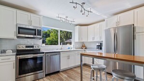 Een moderne keuken met witte kasten, roestvrijstalen apparatuur, een houten aanrecht en een groot raam.