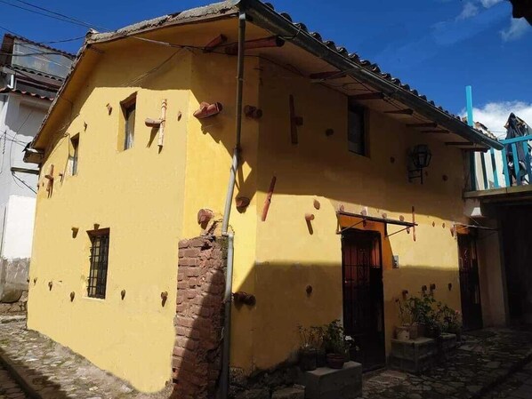 A yellow building with a tiled roof, a brick wall, and a small window.