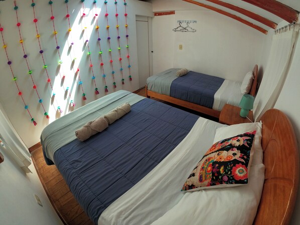 A room with two beds, a wooden ceiling, a wall-mounted hanger, and a window with sunlight.
