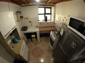 A compact kitchen with a gas stove, a microwave, and a refrigerator. There is a window above the sink, and the walls are tiled.