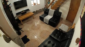 Un salon avec un canapé noir, un banc en bois et un téléviseur fixé au mur.